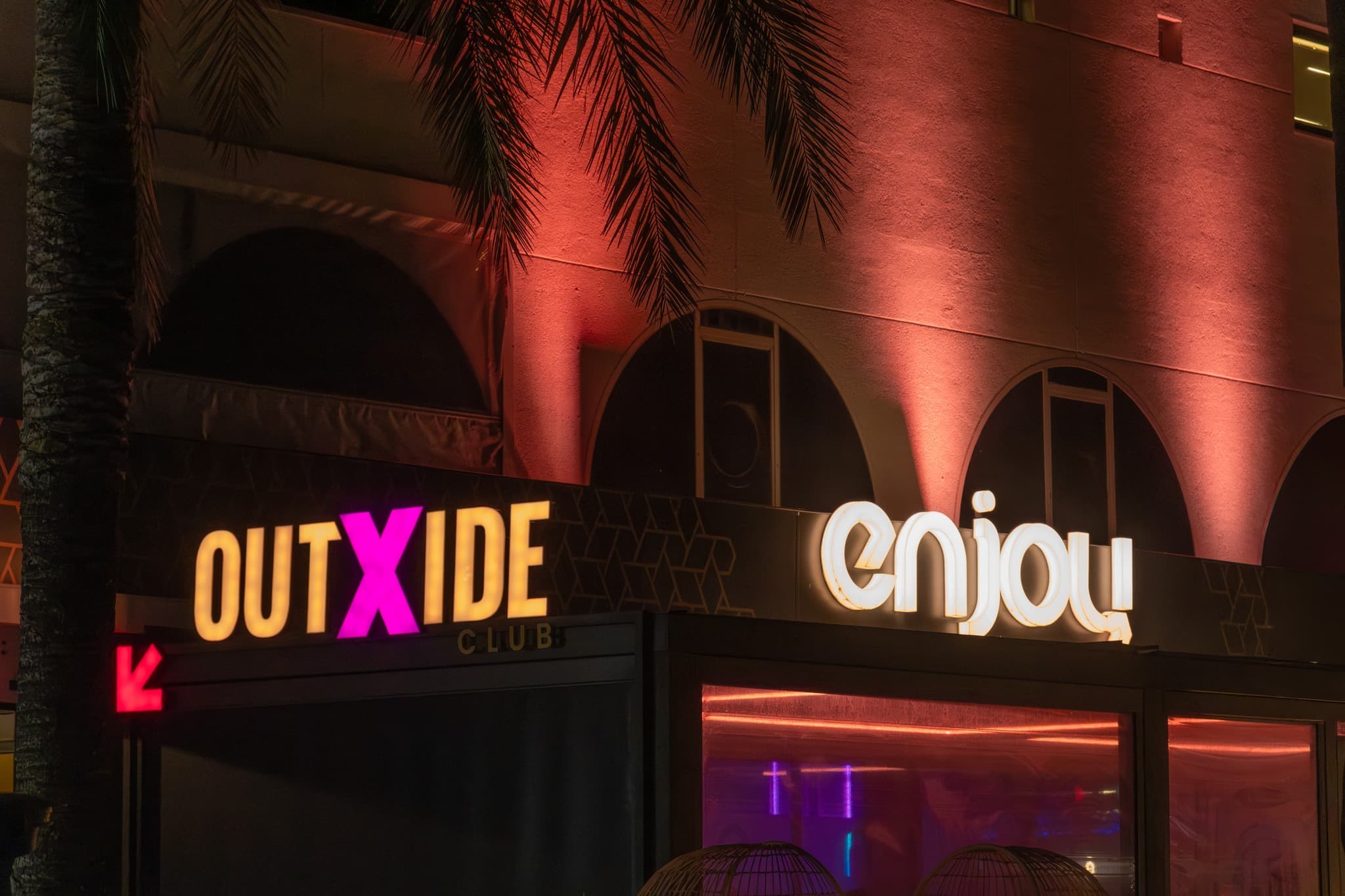 Fachada de OUTXIDE Club y Enjoy Terrace de noche, en la Av. Tucán 1 de Port d'Alcúdia
